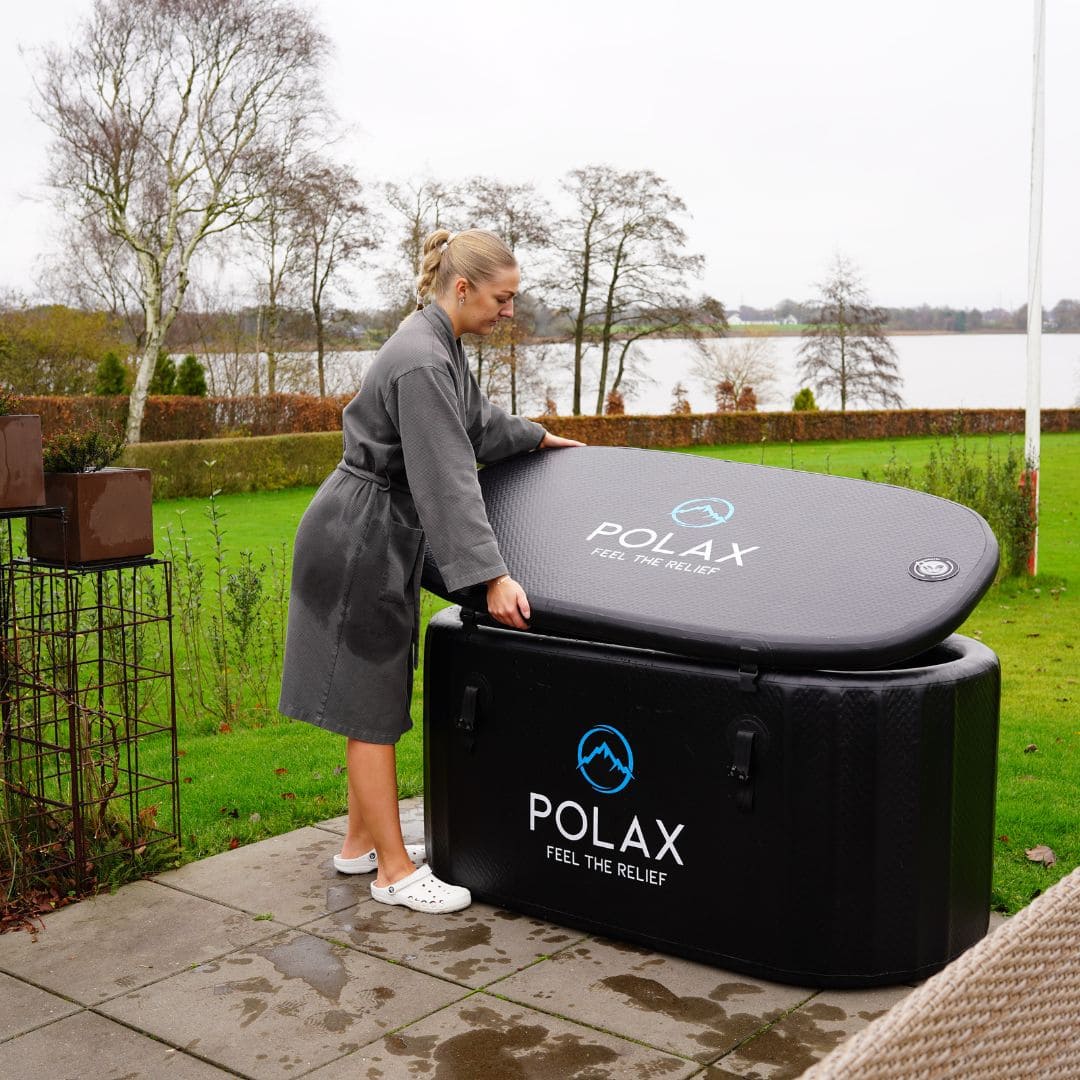 Kvinna i grå badrock lägger locket på Polax Isbad Pro™ i trädgården, en hållbar isbadstunna designad för maximal komfort